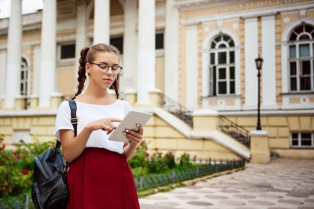 young beautiful female student in glasses looking at tablet outdoors.